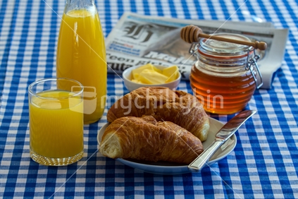 Breakfast scene with croissants, orange juice and honey. NZ herald in the background