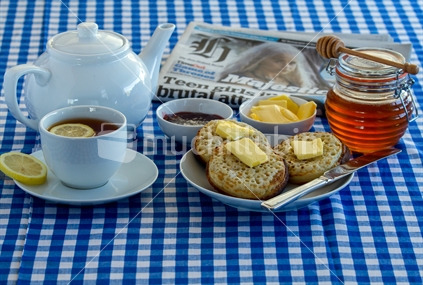 Breakfast scene with crumpets, cup of tea with jam and honey. Newspaper in the background.