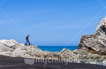 New Zealand man (30 years) walking along beach with blue sky, White Rock, Wairarapa