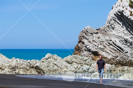 New Zealand man (30 years) walking along beach with blue sky, White Rock, Wairarapa