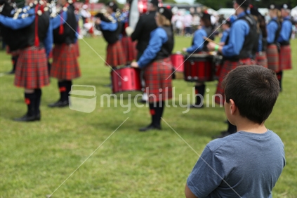 At the annual Hororata Highland Games in mid-Canterbury, a young boy watches from a distance as a highland pipe band proceeds to commence their performance.