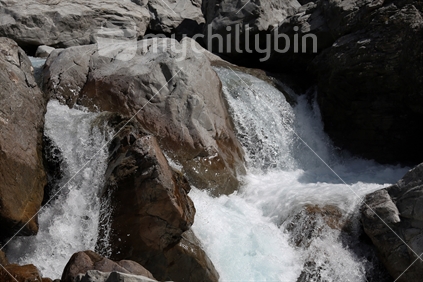 Near to the Otira Viaduct within Arthurs Pass National Park (South Island high country), fresh water flows over rocks and boulders in an alpine river, rushing and splashing.
