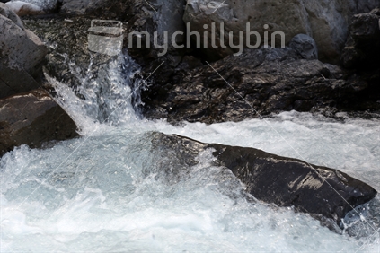 Near to the Otira Viaduct within Arthurs Pass National Park (South Island high country), fresh water flows over rocks and boulders in an alpine river, rushing and splashing.