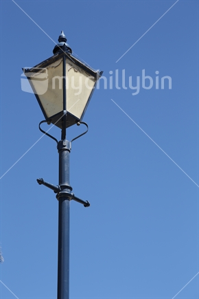 An old-fashioned ornate lamplight with cobwebs set against a clear blue sky.