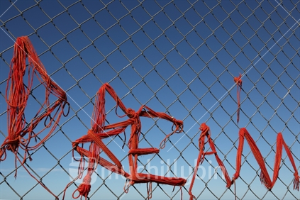 At a Christchurch beach, the word "Dream" is twisted with red wool into a wire mesh security fence, perhaps as an expression of a new future for Christchurch city.