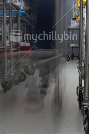 The motion blur of an operating theatre staff member can be seen, as a theatre trolley with clean surgical instrument sets is pushed through an operating theatre set-up room.
