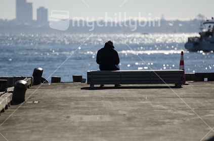 A man sitting at the end od a wharf, watching a ferry in Auckland.