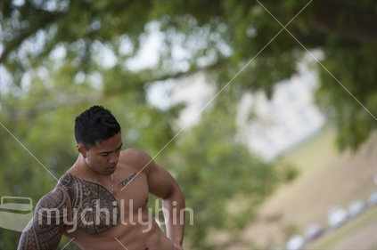 Samoan, Pacific Island body builder with his shirt off in a park setting.
