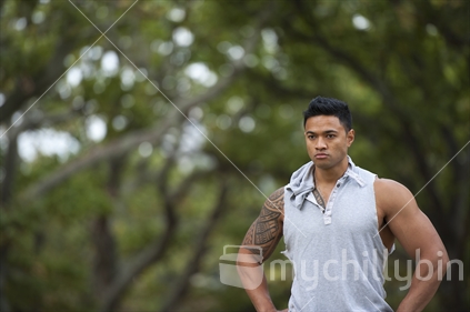 Samoan, Pacific Island body builder with his shirt on in a park setting.