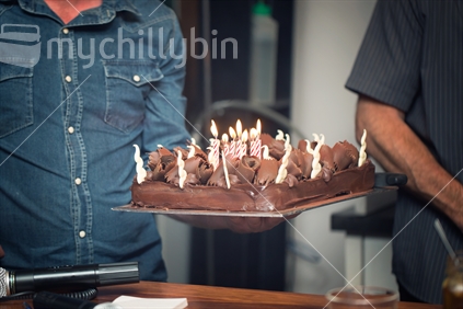 A man holding up a birthday cake, with lit candles.