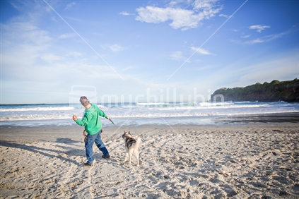 A man about to throw the ball for his two dogs on the beach.