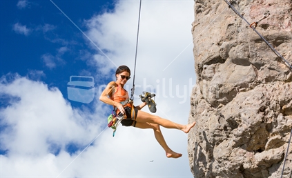 The relaxed descent of a woman as she rappels down from the top of her climb (some motion blur)