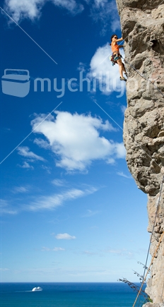 A woman rock climbs one of the faces on Mt Maunganui against the back drop of the sea (raised ISO)
