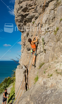 A woman rock climbs one of the faces on Mt Maunganui against the back drop of the sea