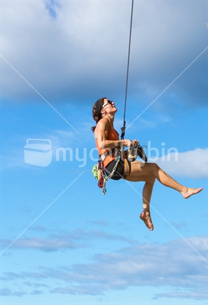 A woman rock climber makes a relaxed descent as she rappels downwards of Mt Maunganui (raised ISO)