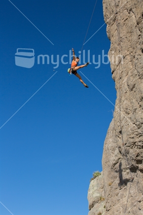 A woman rock climber star jumps as she rappells down from her climb on the rock face of Mt Maunganui (some motion blur)