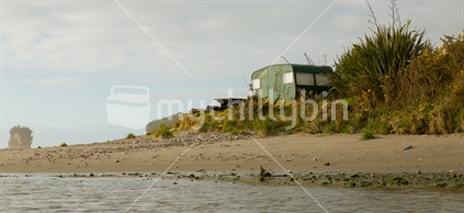 Gorse, flax, and an old caravan nestles on the shore of Pororari lagoon at Punakaiki on the West Coast of the South Island