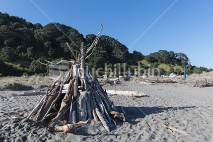 A driftwood tent structure leads the way to the Ohiwa Camping Ground from the beach