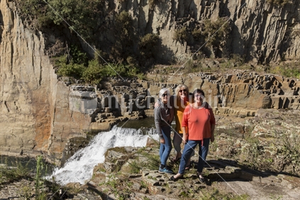 Three mature ladies on the edge of the Aniwhenua falls on a sunny autumn day in Galatea