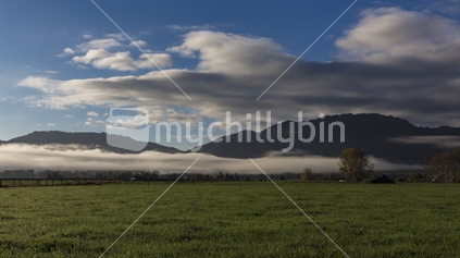 A low band of early cloud hovers around the forested hills and mountains of the Ikawhenua ranges on the Galatea plains
