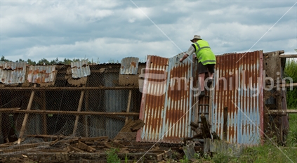 Man in hi-vis vest dismantles an old shed