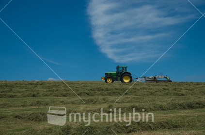 Tractor raking silage into rows.