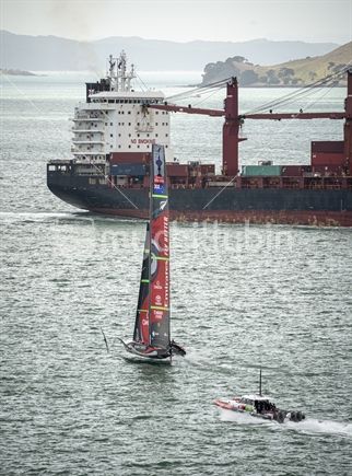 Team NZ Americas Cup yacht sailing around large cargo ship off North Head