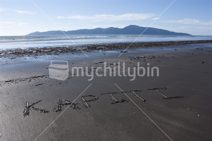'Kapiti' written in the sand with Kapiti Island in the background.  
