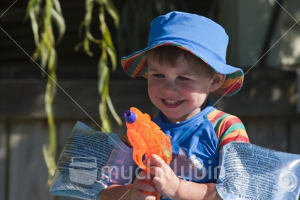 Little boy playing with water gun by backyard swimming pool.  