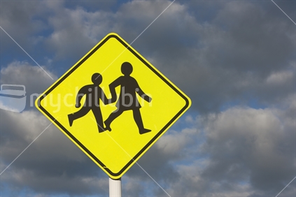 Children crossing sign against a cloudy sky.  