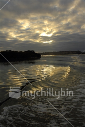 wake of boat caught with reflections in early morning light up Mahurangi River