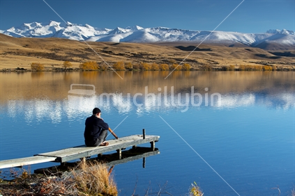 Man plays didgeridoo on jetty overlooking lake