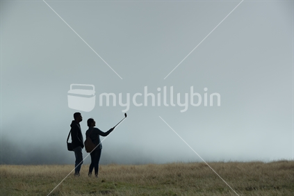 Two people use a selfie stick to take a self portrait amidst the early morning fog