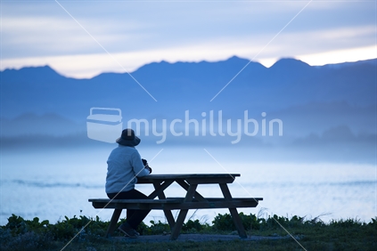 Person sits at a table by the water