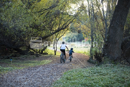 A child and parent riding bikes through a trail in the forest (high ISO)
