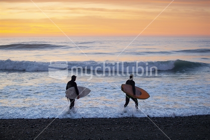 Two surfers wading into the ocean at dawn