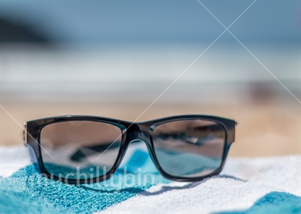 Sun glasses sitting on beach towel with Whangamata Beach in the background