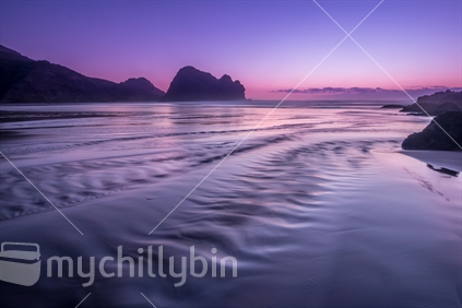 Milky water streaming down sand into Piha ocean next to Lion rock, Piha Beach (artistic treatment)