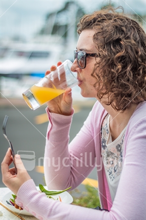 Lady drinking Orange juice at cafe in front of marina