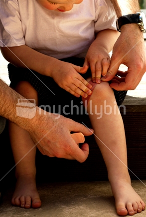 Toddler with father helping put on a plaster.