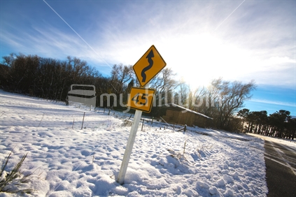 Yellow traffic sign along a rural snowy road in New Zealand