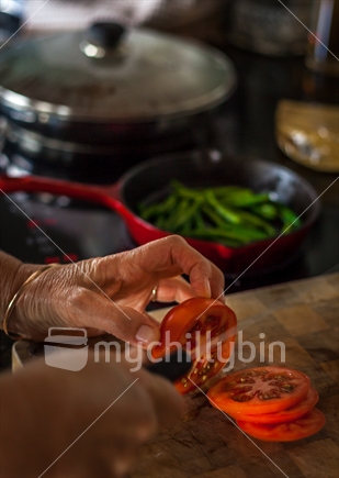 Chopping tomatoes in preparation for a meal cooking in the background