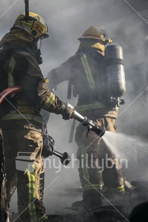 Two Firemen fighting house fire with a hose 