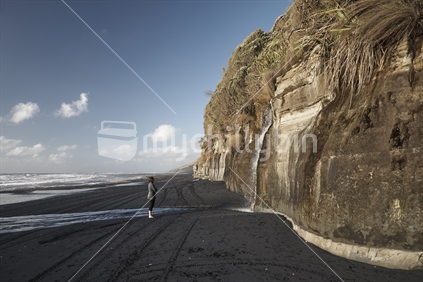 Woman watching a waterfall falling over a cliff on a black sand beach of the West Coast - Mokau, North Island