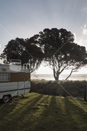 Typical camping scene with an old caravan and Pohutukawa tree on the waterfront of Mokau on the West Coast, North Island