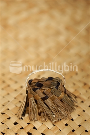 Mini flax kete with flax weaving background