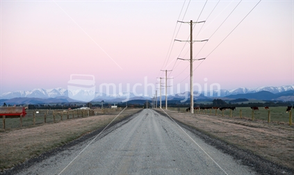 Morning view of farmland with gravel road and snowy mountains