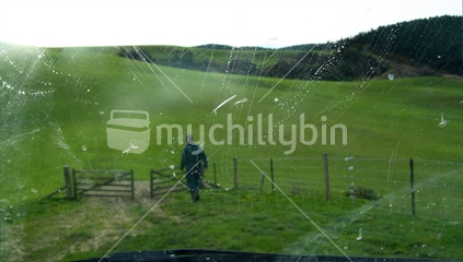A farmer at work shutting a gate, viewed through a muddy truck window,