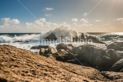 Man on rocks with arms out facing the ocean waves