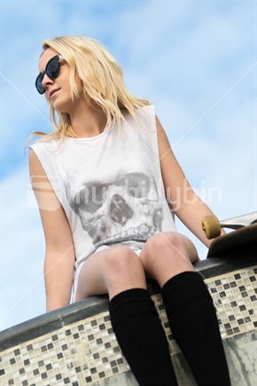 Blond teenage girl sitting next to skateboard